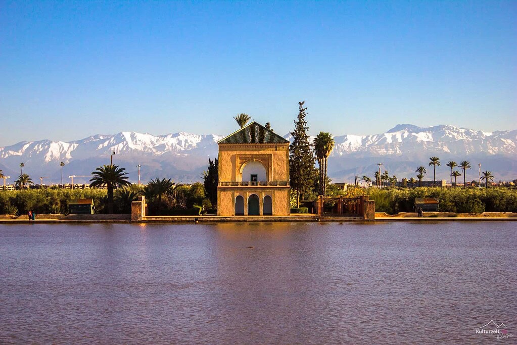 Kulturreisen Marrakesch 2027: Pavillon im Menara-Garten mit Wasserbecken und Hohem Atlas im Hintergrund.