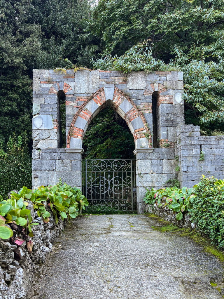 Reise Programm Comersee 2026 14 Historisches Eingangsportal aus Stein mit gotischem Spitzbogen aus rotem Backstein und schmiedeeisernem Tor in einem Garten am Comersee – Kulturzelt Reisen Kultur- und Gartenreise Comersee 2026
