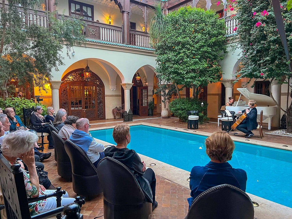 KULTURZELT REISEN 7 Cellist und Pianistin am weissen Flügel spielen am Pool eines Riad-Innenhofs, die Reisegäste sitzen im Halbkreis