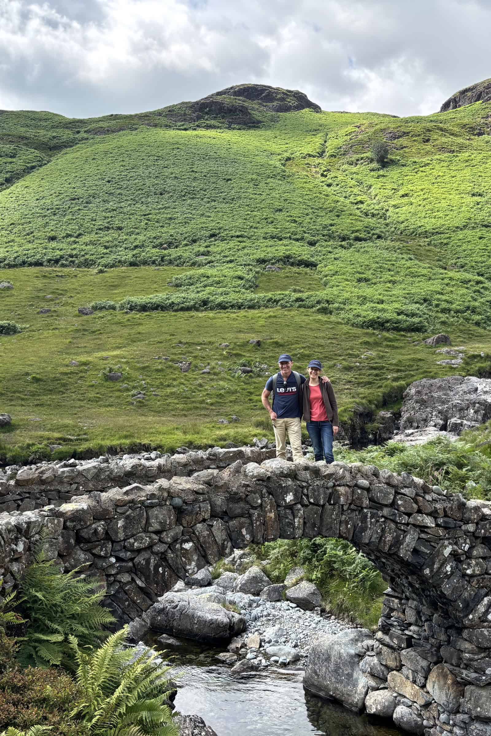 Vorschau Lake District 2028 5 Andreas C. Fischer und Nadja Saminskaja auf einer alten Steinbogenbrücke im Lake District, dahinter ein grüner Fell