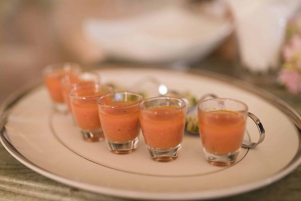 KULTURZELT REISEN 28 Kleine Gläser mit Gazpacho auf einem hellen Porzellanteller mit Silberrand